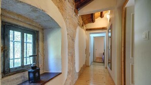 Ein schmaler Flur mit Holzboden, einer rustikalen Steinwand und einem Fenster mit einem kleinen Tisch.