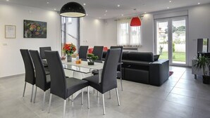 Ein modernes Wohnzimmer mit einem Glastisch, schwarzen Stühlen, einer schwarzen Couch und einer roten Pendelleuchte.