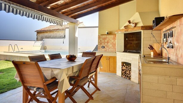 Cocina exterior con comedor, horno empotrado y vista al mar.