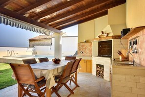 Une cuisine extérieure avec un espace repas, un four encastré et une vue sur la mer.