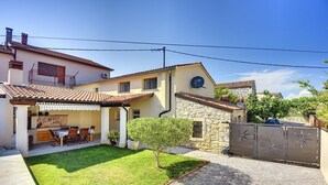 Una casa de dos pisos con un patio, un césped pequeño y un muro de piedra.