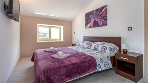 Un dormitorio con una cama, una mesita de noche, una lámpara, un ventanal y un cuadro en la pared.