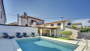 Una piscina con sillas de descanso, un muro de piedra y un pequeño jardín.
