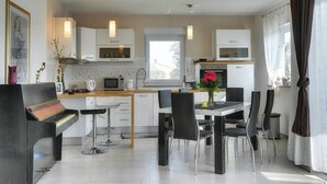 A modern kitchen with white cabinets, a dining area with black chairs, and a piano. - Villa Amber (V3551-K1) - Vodnjan (Vodnjan)