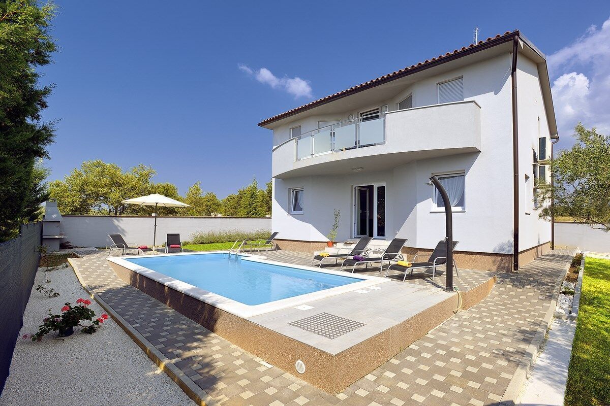 A two-story house with a swimming pool, outdoor seating, and a garden.