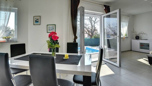 A modern living room with a dining area, large windows, and a view of a swimming pool. - Villa Amber (V3551-K1) - Vodnjan (Vodnjan)
