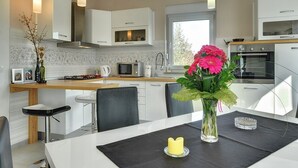 A modern kitchen with white cabinets, a dining area with a table, chairs, and a vase with flowers. - Villa Amber (V3551-K1) - Vodnjan (Vodnjan)
