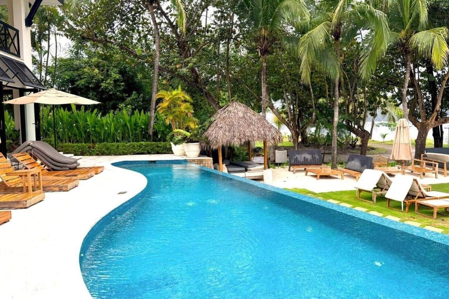 Une piscine avec des chaises longues et une structure surmontée d’un toit de chaume.