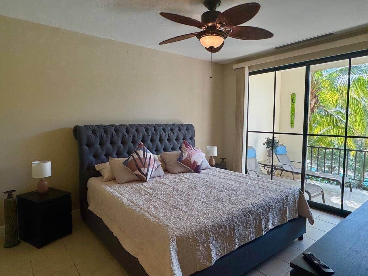 A bedroom with a large bed, a ceiling fan, and a view of the outdoors through a sliding glass door.