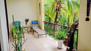 A balcony with a chair, a small table, and potted plants. - Cozy 1BDR Condo pool front in Playas del Coco (Coco)