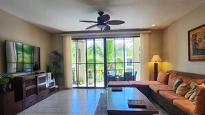 A spacious living room with a flat-screen TV, a sofa, a coffee table, and a ceiling fan. - Cozy 1BDR Condo pool front in Playas del Coco (Coco)