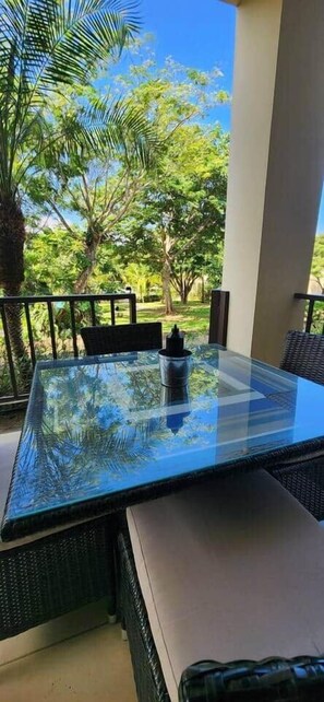 A glass-top table with wicker chairs on an outdoor patio with a view of trees. - Pacífico L802 - 2BDR Easy Access, Great Location (Coco)