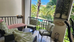 A balcony with wicker furniture, a small table, and a decorative wall with a tree silhouette and a welcome sign. - Wake Up in Paradise, Amazing 3BDR Condo Near Beach (Coco)