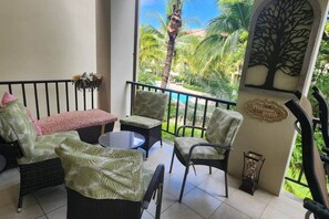 Ein Balkon mit Korbmöbeln, einem kleinen Tisch und einer Wand mit Baumkontur und Willkommensschild.