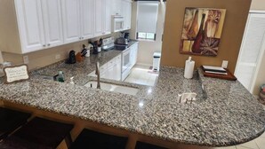 A kitchen with white cabinets, granite countertops, and a central island with a sink. - Wake Up in Paradise, Amazing 3BDR Condo Near Beach (Coco)