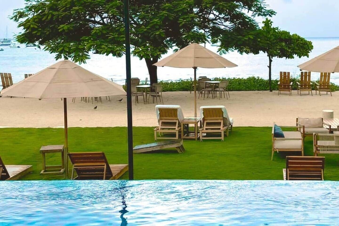 A poolside area with lounge chairs and umbrellas, a grassy lawn, and a view of the beach and ocean.