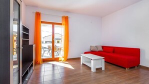 Ein modernes Wohnzimmer mit einem roten Sofa, einem weißen Couchtisch und einer Glastür, die zu einem Außenbereich führt.