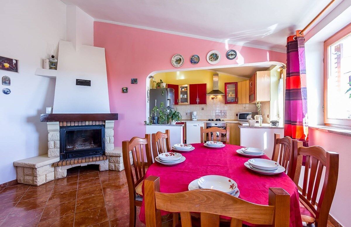 A dining area with a red tablecloth, wooden chairs, and a fireplace.
