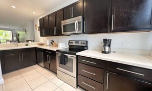 A modern kitchen with dark cabinets, stainless steel appliances, and a white countertop. - 3 BDR 2 bath Luxurious CONDO, Pool Front (Coco)