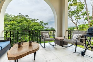 Ein Balkon mit Korbmöbeln, einem Holztisch und einem Grill.
