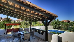 Un patio exterior con piscina, suelo de piedra y una estructura de pérgola.
