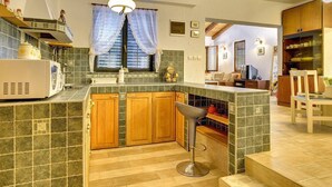 Una cocina con armarios de madera, un taburete de bar, un microondas y una ventana con cortinas.