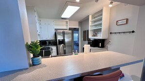 Una cocina moderna con armarios blancos, electrodomésticos de acero inoxidable y una encimera con dos sillas rojas.