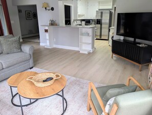 En moderne stue med en grå sofa, et træbord og et tv på et sort stativ.