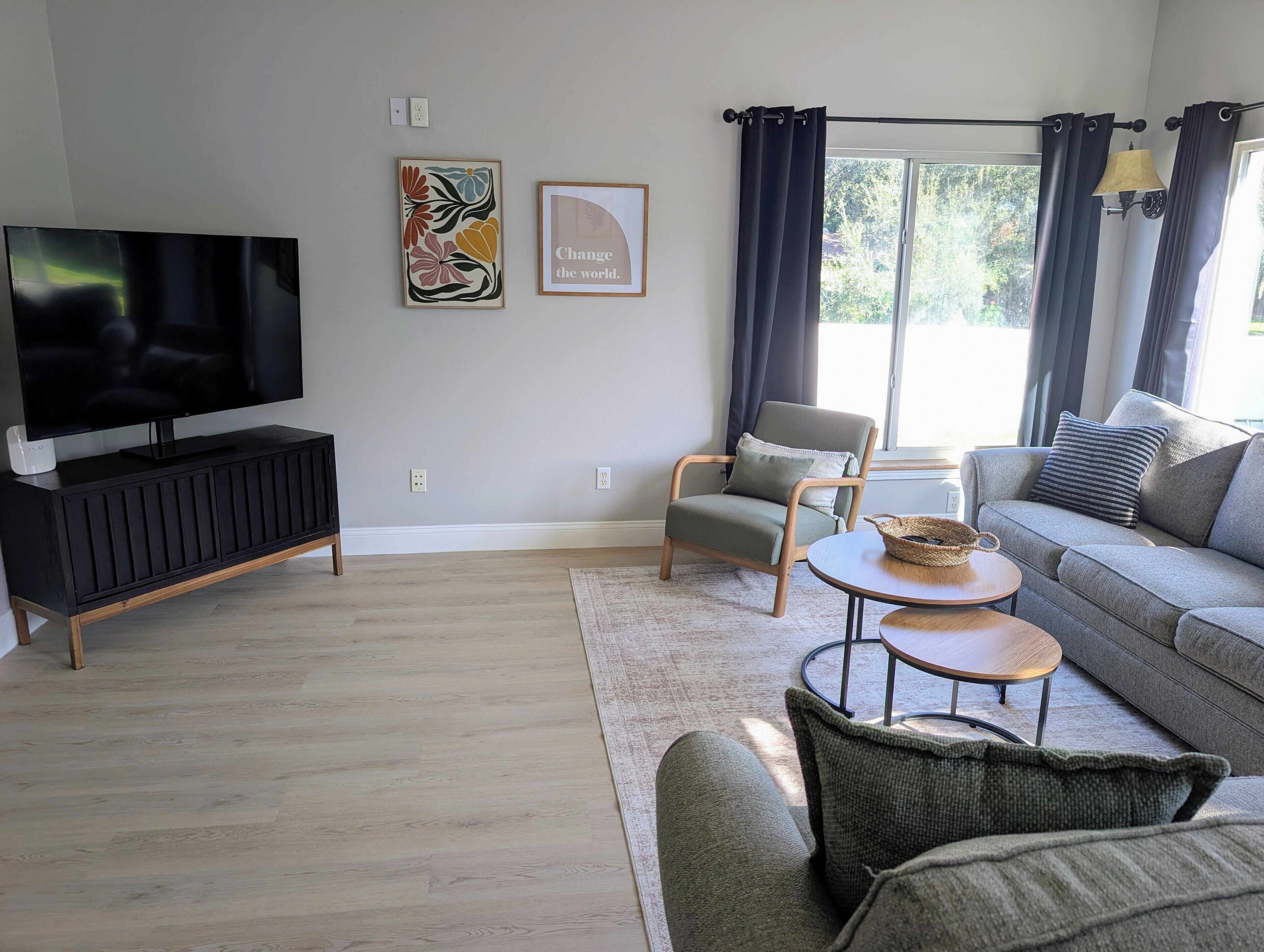 A modern living room with a flat-screen TV, a grey sofa, a wooden coffee table, and a grey armchair.