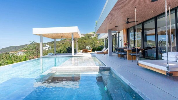 Ein moderner Infinity-Pool mit weißer Liegefläche, Gartenmöbeln und Blick auf die Hügel.