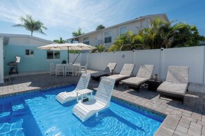 Ein Swimmingpool mit Liegestühlen und einem Tisch, umgeben von einem weißen Zaun und Palmen.