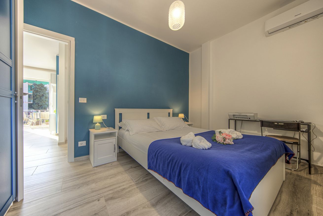 A bedroom with a bed, bedside tables, a desk, and an air conditioning unit.