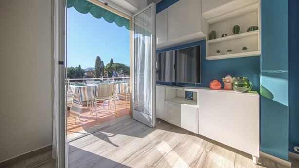 A modern kitchen with a TV, white cabinets, and a balcony with a table and chairs. - CASA PIOPPI - Comfort and a beautiful view (Rapallo)