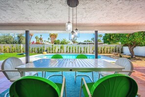 An outdoor pool area with a table and chairs, surrounded by a white fence and greenery. - 3BR Mid-Century Home Pool, Hot Tub & Gym (Palm Springs)