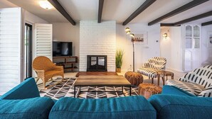 Ein Wohnzimmer mit Kamin aus weißem Backstein, modernen Möbeln und freiliegenden Holzbalken.