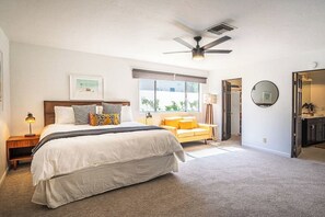 A bedroom with a large bed, a ceiling fan, a window with blinds, a bedside table with a lamp, and a view of the outside. - 3BR Mid-Century Home Pool, Hot Tub & Gym (Palm Springs)