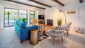 Ein modernes Wohnzimmer mit einem blauen Sofa, gemusterten Sesseln, einem Kamin und einem Fernseher.