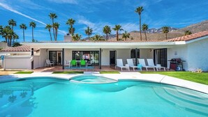Ein modernes Haus mit Swimmingpool, Sitzgelegenheit im Freien und Palmen.