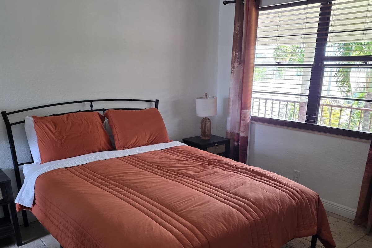 Een bed met een bruine sprei, een wit kussen en een nachtkastje met een lamp.