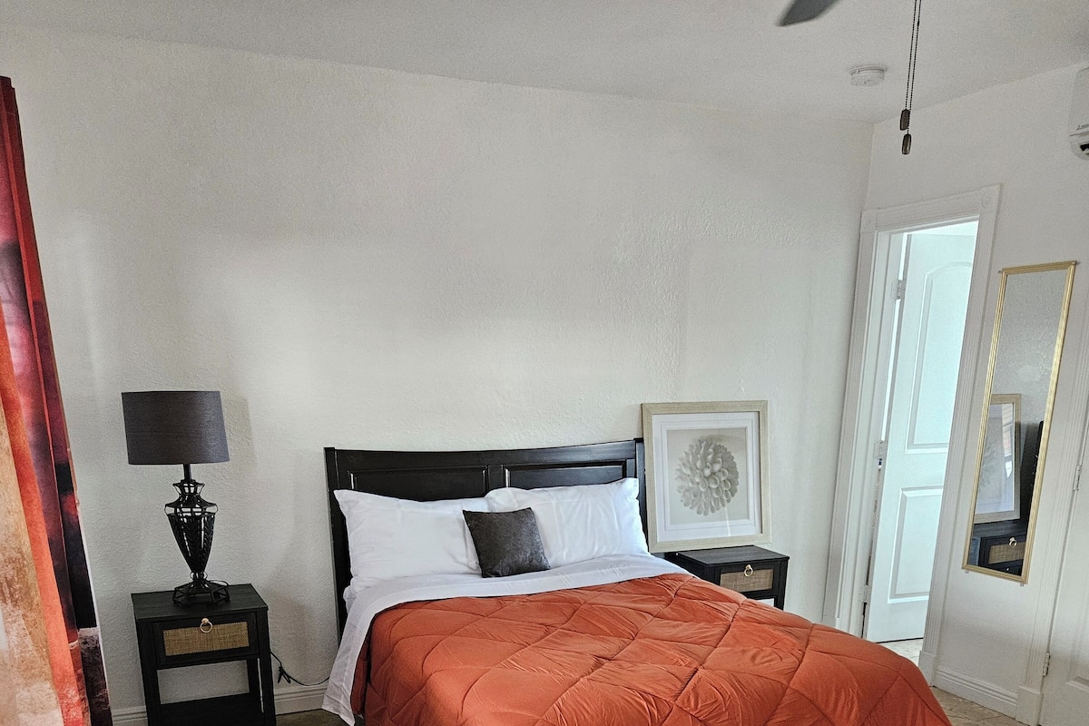 Een slaapkamer met een bed, nachtkastjes, een lamp, een spiegel en een deur.