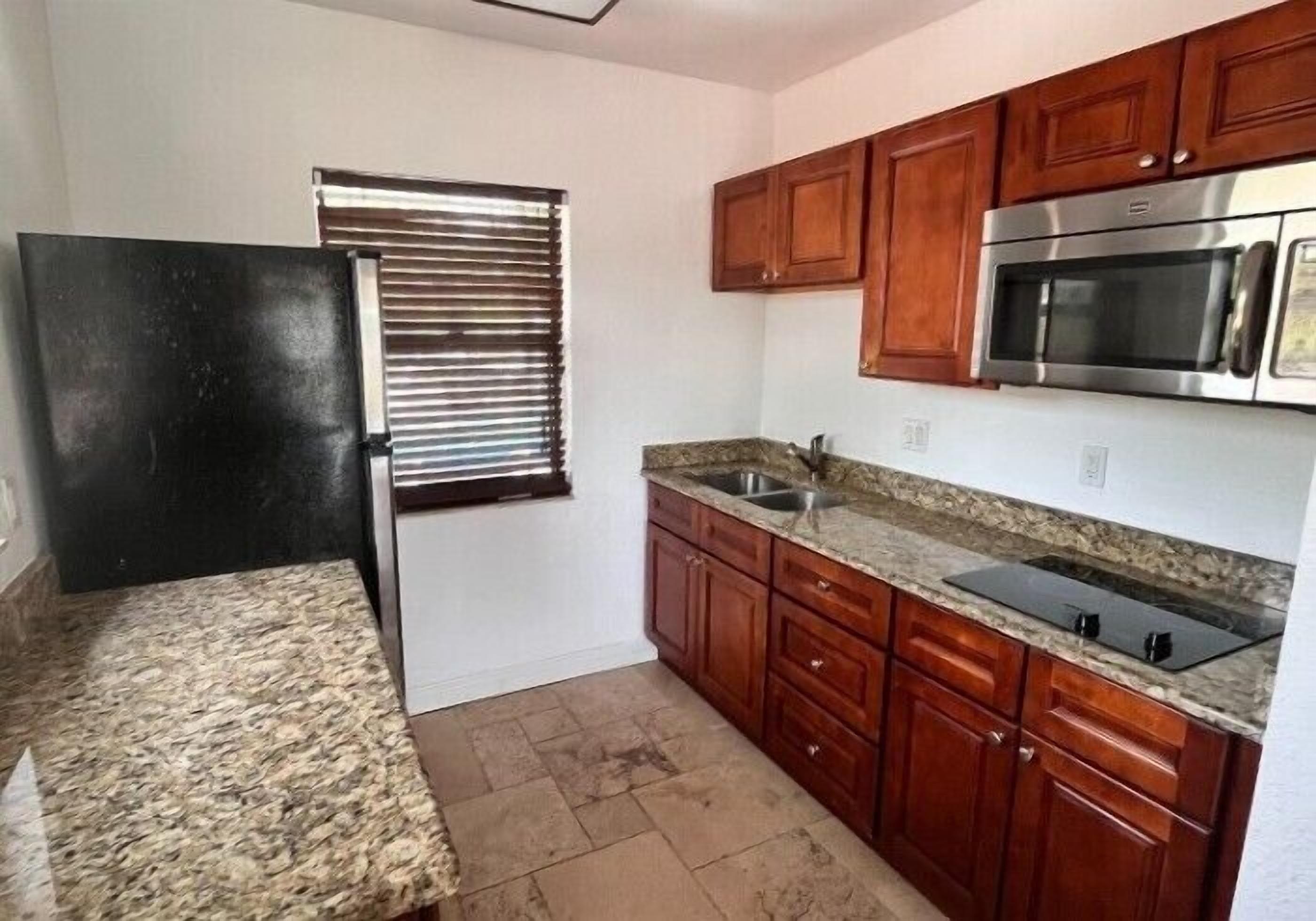 A kitchen with wooden cabinets, a stainless steel microwave, and a granite countertop.