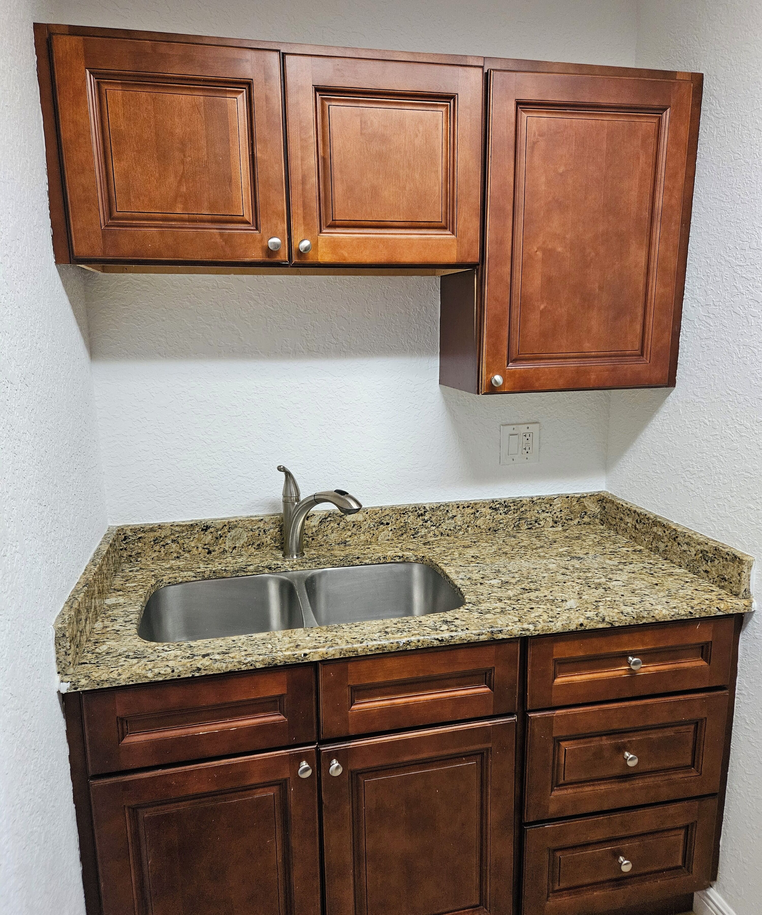 A kitchen with granite countertops, a stainless steel sink, and wooden cabinets.