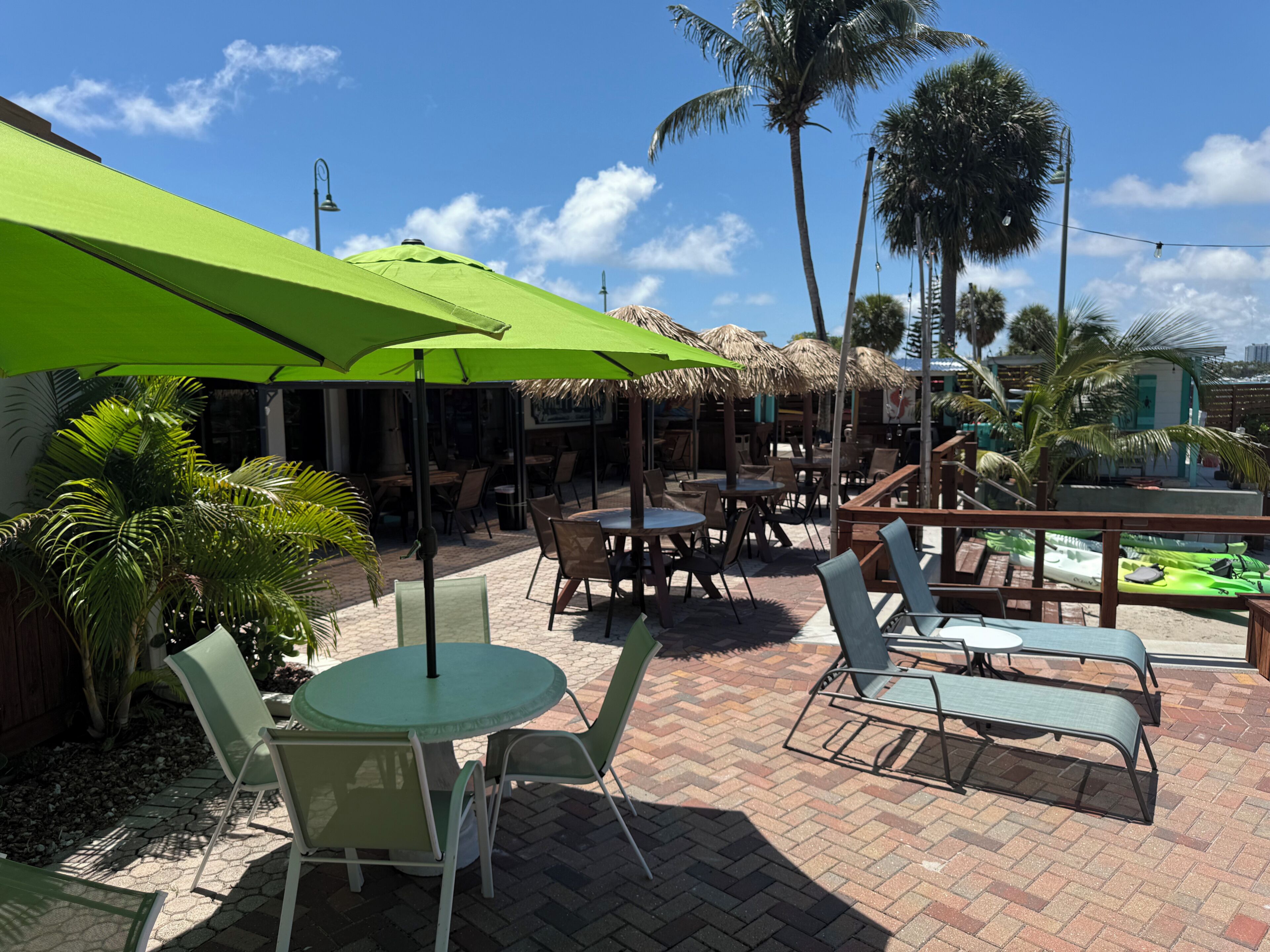 An outdoor patio with tables and chairs, umbrellas, and palm trees.