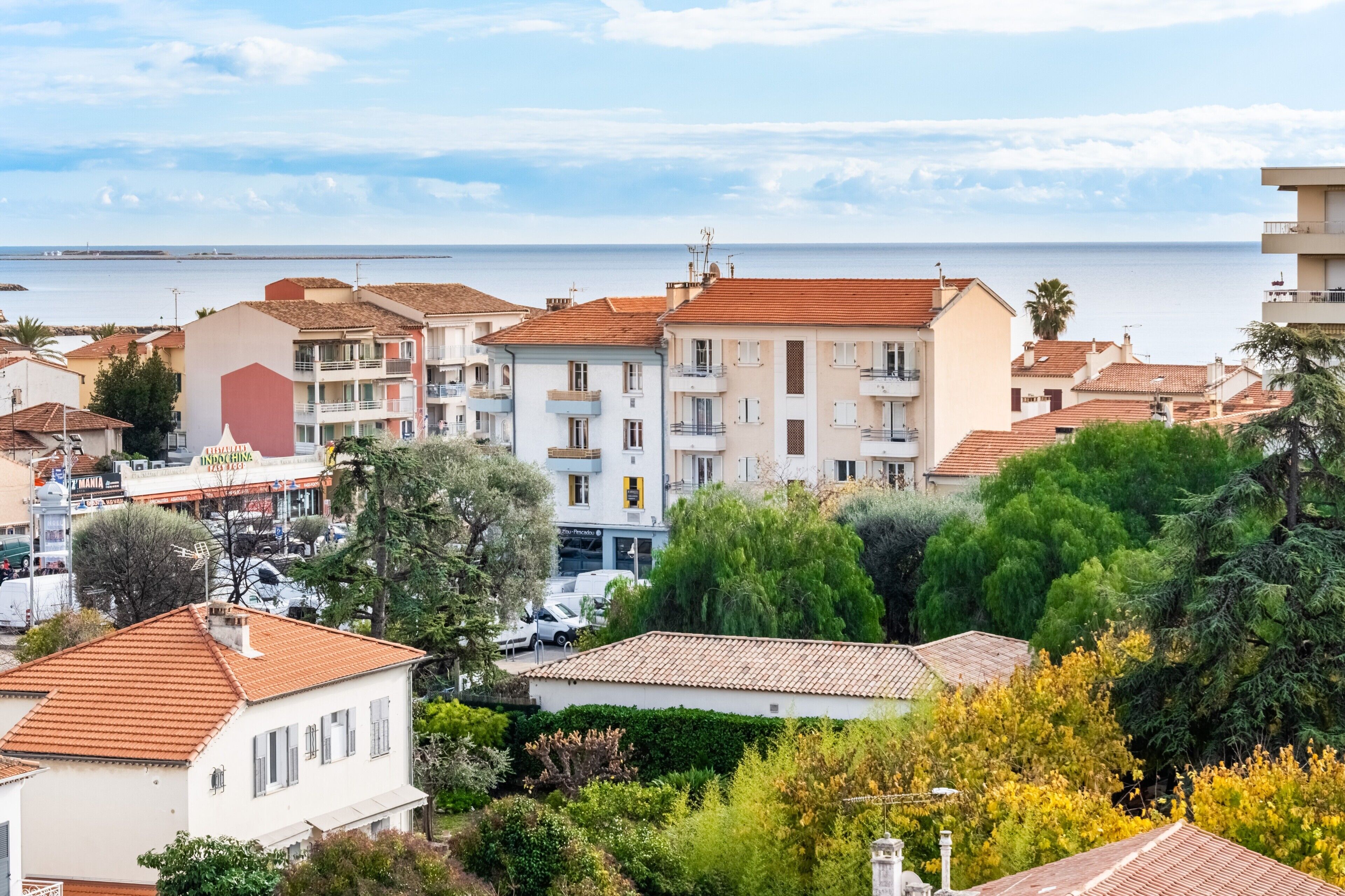 Una zona residenziale costiera con edifici a più piani, un porto turistico ben visibile e una limpida vista sul mare.