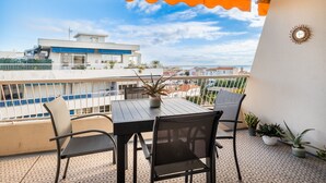 En balkon med et bord, stole, plantekasser og udsigt til bygninger.