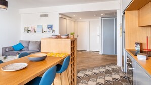Et moderne køkken med træbordplade, et spiseområde med bord og stole, samt en grå sofa med blåt pudebetræk.