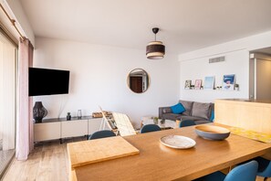 Ein modernes Wohnzimmer mit Esstisch, Sofa und einem flachbildfernseher an der Wand.