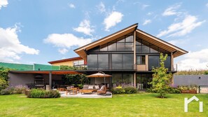 A modern two-story house with a large glass facade, a covered patio with outdoor furniture, and a well-maintained garden. - Casa Gala With spectacular valley view (Valle de Bravo)