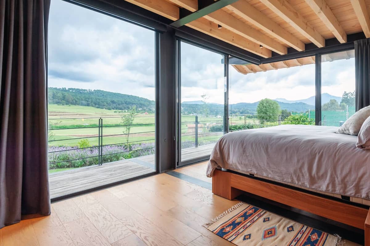 Une chambre avec une grande fenêtre, un plafond en bois et un lit doté d’une tête de lit.