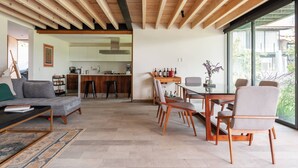Un soggiorno moderno con divano, tavolino e zona pranzo con sedie e tavolo. Sullo sfondo, una cucina con bancone e sgabelli.